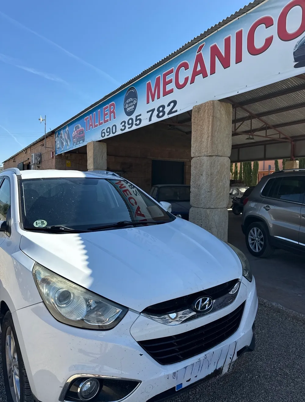 Fachada del taller con el cartel y un coche esperando en la entrada.