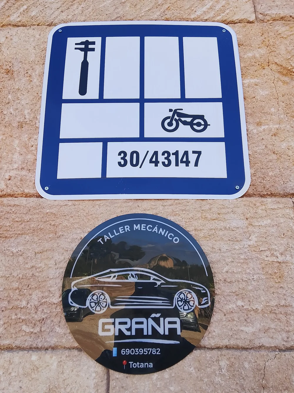 Placa oficial de taller número 30/43147 atornillada en la fachada, junto al disco del logotipo de Taller Graña.